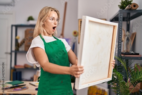 Young caucasian woman looking at canvas afraid and shocked with surprise and amazed expression, fear and excited face.