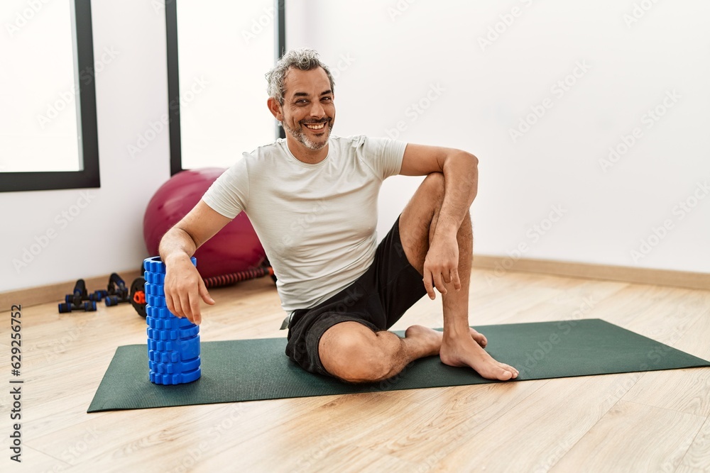 Middle age grey-haired man smiling confident leaning on foam roller at sport center Middle age grey-haired man smiling confident leaning on foam roller at sport center