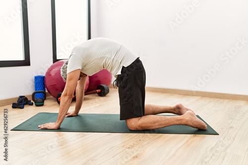 Middle age grey-haired man stretching back at sport center