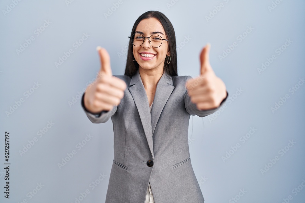 Hispanic business woman wearing glasses approving doing positive gesture with hand, thumbs up smiling and happy for success. winner gesture. Hispanic business woman wearing glasses approving doing positive gesture with hand, thumbs up smiling and happy for success. winner gesture.