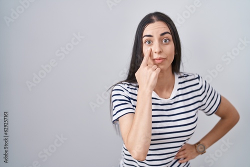 Young brunette woman wearing striped t shirt pointing to the eye watching you gesture, suspicious expression
