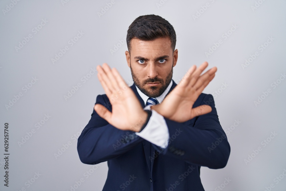 Handsome hispanic man wearing suit and tie rejection expression crossing arms and palms doing negative sign, angry face Handsome hispanic man wearing suit and tie rejection expression crossing arms and palms doing negative sign, angry face