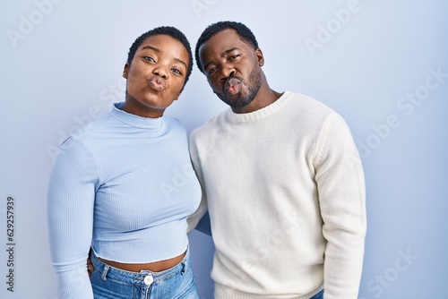 Young african american couple standing over blue background looking at the camera blowing a kiss on air being lovely and sexy. love expression.