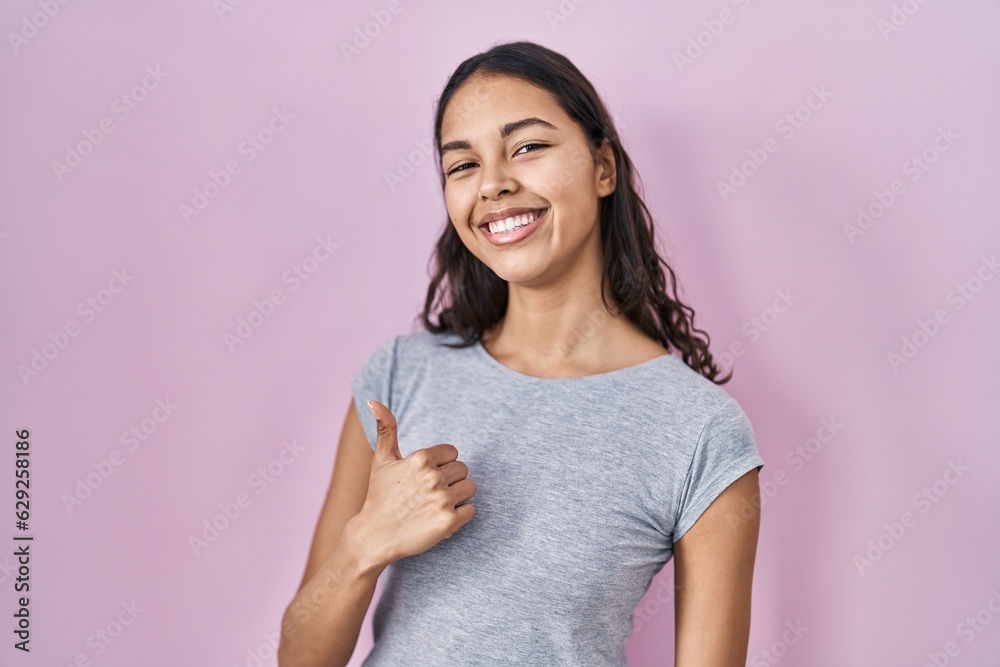 Fototapeta premium Young brazilian woman wearing casual t shirt over pink background doing happy thumbs up gesture with hand. approving expression looking at the camera showing success.