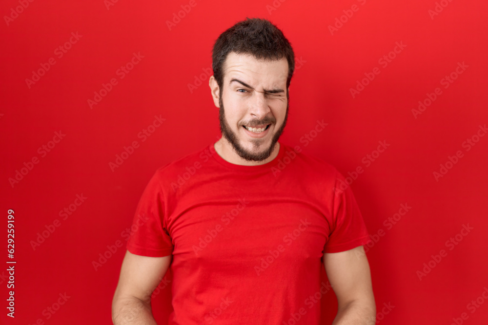 Young hispanic man wearing casual red t shirt winking looking at the camera with sexy expression, cheerful and happy face. Young hispanic man wearing casual red t shirt winking looking at the camera with sexy expression, cheerful and happy face.