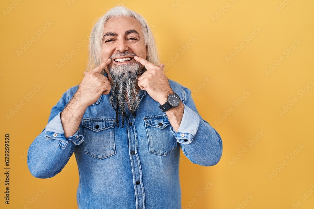 Middle age man with grey hair standing over yellow background smiling with open mouth, fingers pointing and forcing cheerful smile