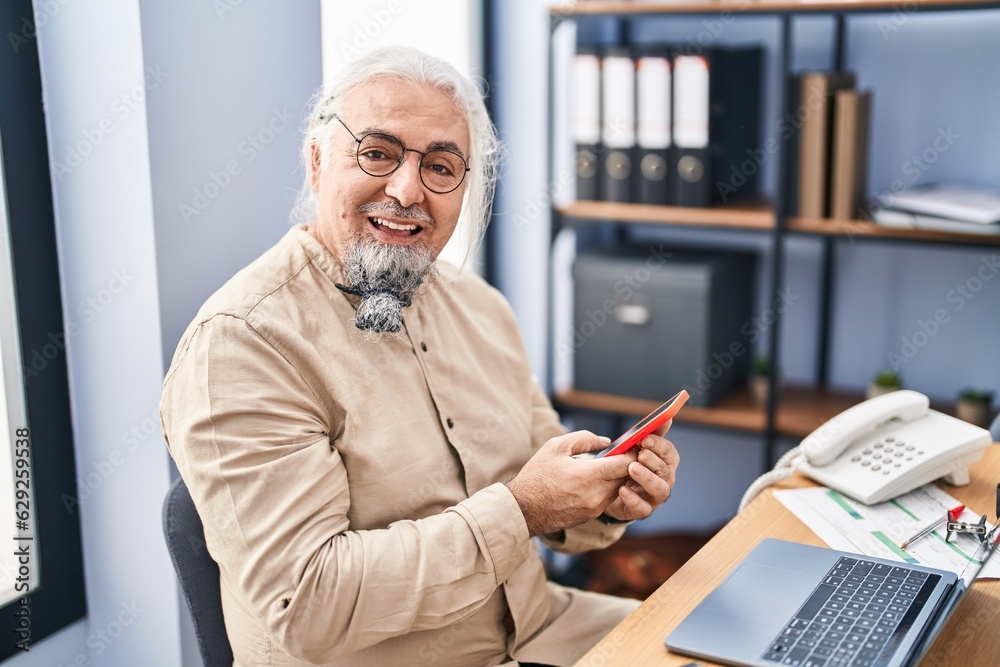 Middle age grey-haired man business worker using laptop and smartphone at office Middle age grey-haired man business worker using laptop and smartphone at office