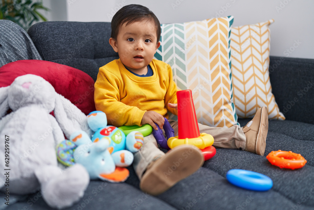 Adorable hispanic boy playing with hoops game sitting on sofa at home Adorable hispanic boy playing with hoops game sitting on sofa at home