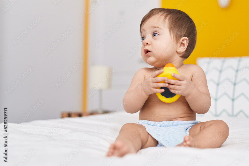 Adorable caucasian baby sitting on bed playing with duck toy at bedroom Adorable caucasian baby sitting on bed playing with duck toy at bedroom
