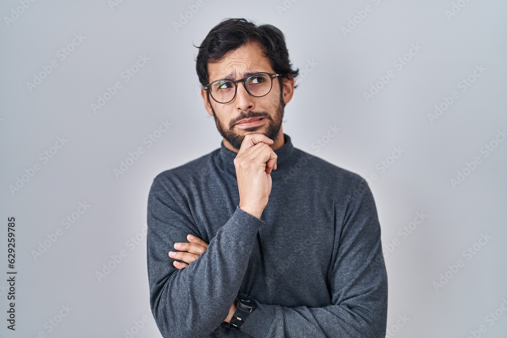 Handsome latin man standing over isolated background thinking worried about a question, concerned and nervous with hand on chin Handsome latin man standing over isolated background thinking worried about a question, concerned and nervous with hand on chin