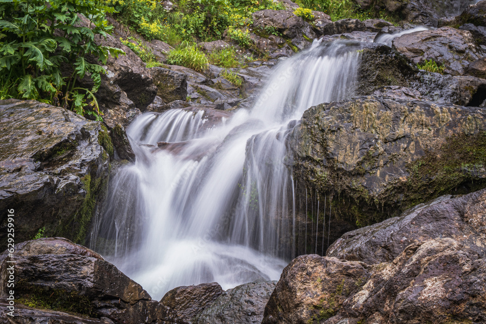 Beautiful waterfall at the mountain with blue sky and white cumulus clouds. Waterfall in tropical green tree forest. Waterfall is flowing in jungle. Nature abstract background. Granite rock mountain.