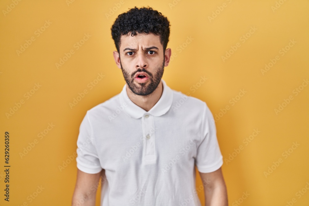 Arab man standing over yellow background afraid and shocked with surprise and amazed expression, fear and excited face. Arab man standing over yellow background afraid and shocked with surprise and amazed expression, fear and excited face.