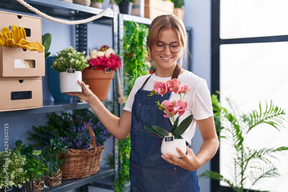 Young blonde girl florist smiling confident holding plant pot at florist
