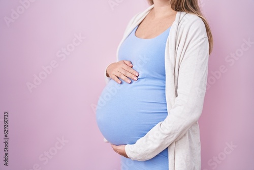 Young pregnant woman expecting a baby, touching pregnant belly looking positive and happy standing and smiling with a confident smile showing teeth