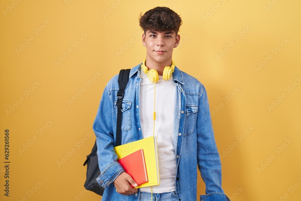 Hispanic teenager wearing student backpack and holding books winking looking at the camera with sexy expression, cheerful and happy face. Hispanic teenager wearing student backpack and holding books winking looking at the camera with sexy expression, cheerful and happy face.