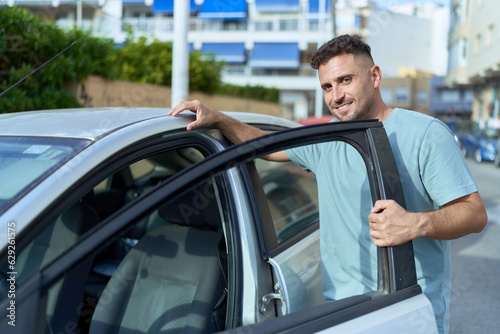 Young hispanic man smiling confident opening car door at street