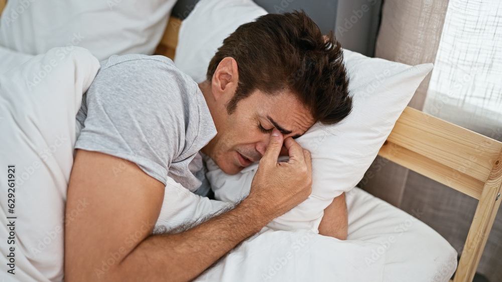 Young hispanic man lying on bed with sad expression crying at bedroom Young hispanic man lying on bed with sad expression crying at bedroom