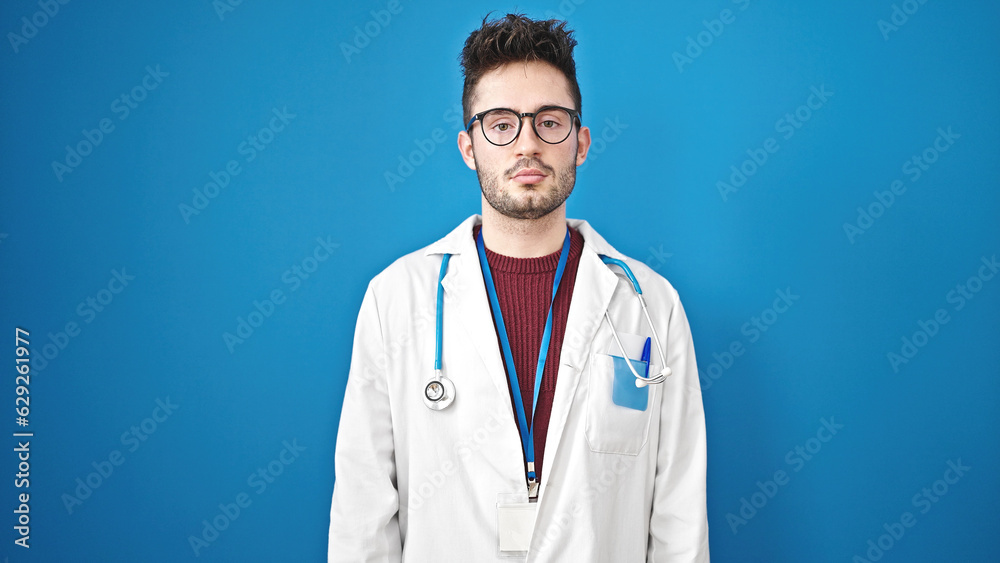 Young hispanic man doctor standing with serious expression over isolated blue background Young hispanic man doctor standing with serious expression over isolated blue background