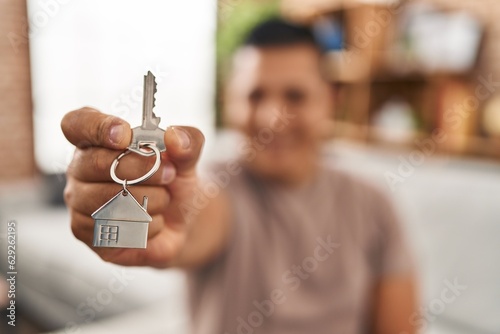 Young latin man holding key of new house sitting on sofa at home