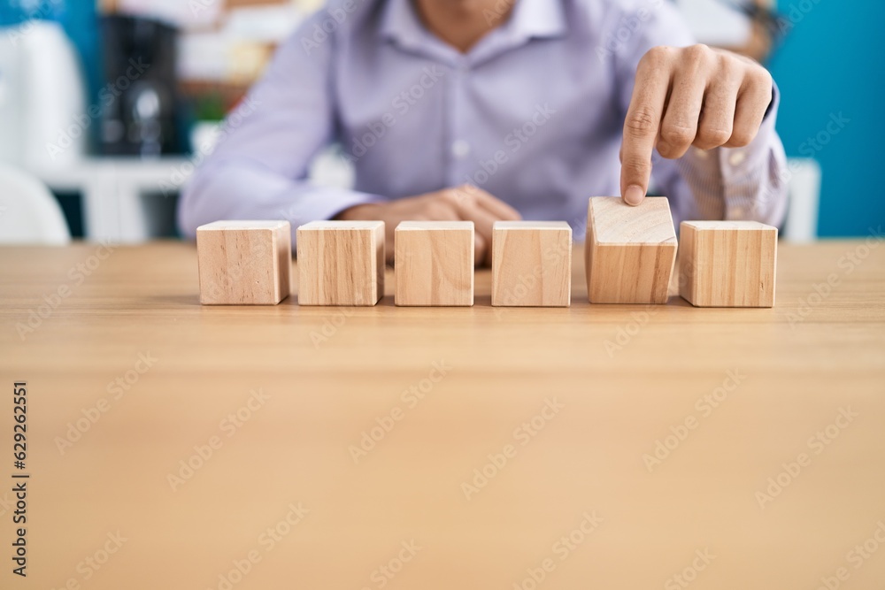 Young hispanic man business worker sitting on table with wooden cubes at office Young hispanic man business worker sitting on table with wooden cubes at office