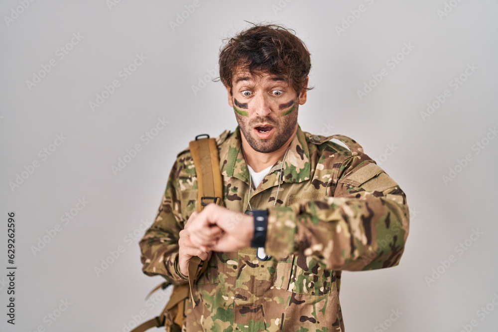 Hispanic young man wearing camouflage army uniform looking at the watch time worried, afraid of getting late