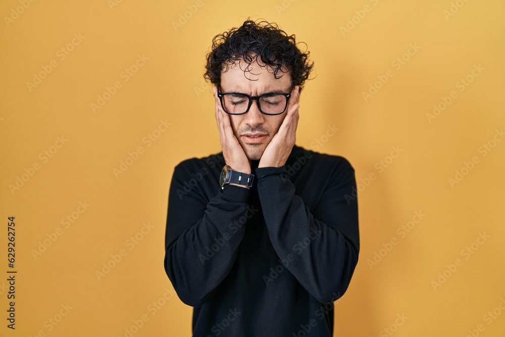 Hispanic man standing over yellow background with hand on head, headache because stress. suffering migraine. Hispanic man standing over yellow background with hand on head, headache because stress. suffering migraine.