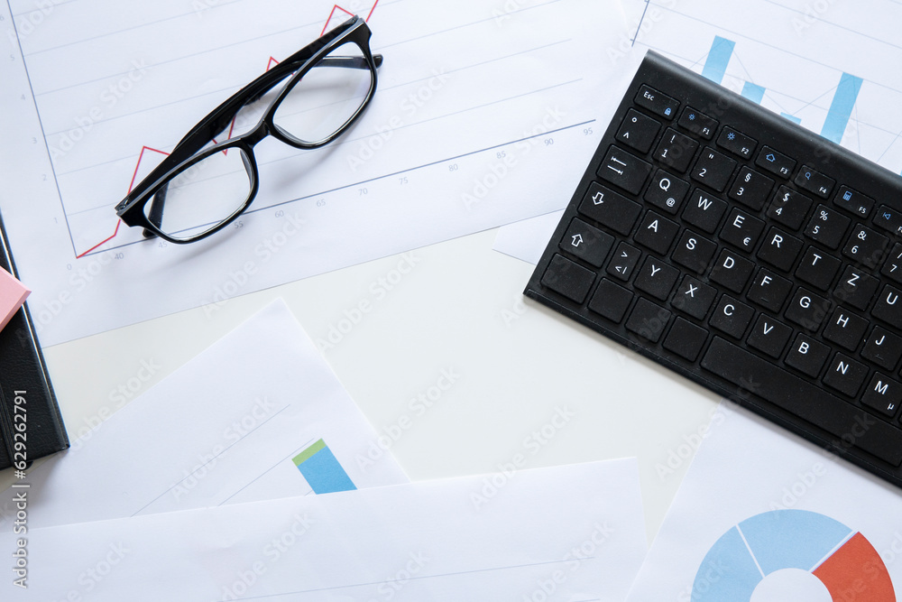 Lots of charts, keyboard, glasses on the desktop. Top view, flat lay Lots of charts, keyboard, glasses on the desktop. Top view, flat lay