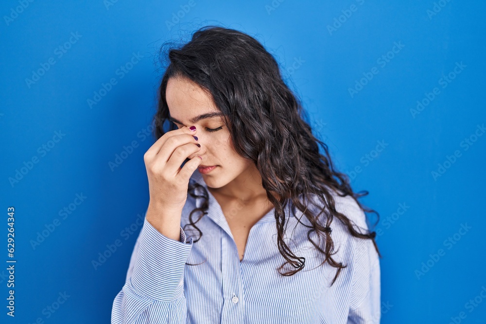 Young brunette woman standing over blue background tired rubbing nose and eyes feeling fatigue and headache. stress and frustration concept. Young brunette woman standing over blue background tired rubbing nose and eyes feeling fatigue and headache. stress and frustration concept.