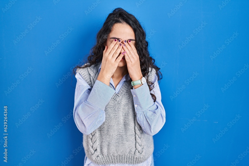 Young brunette woman standing over blue background rubbing eyes for fatigue and headache, sleepy and tired expression. vision problem Young brunette woman standing over blue background rubbing eyes for fatigue and headache, sleepy and tired expression. vision problem