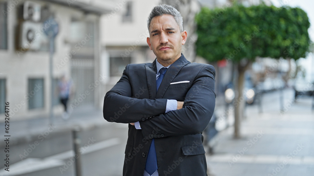 Young hispanic man business worker standing with serious face and arms crossed gesture at street