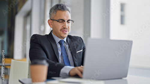 Young hispanic man business worker wearing glasses using laptop at office