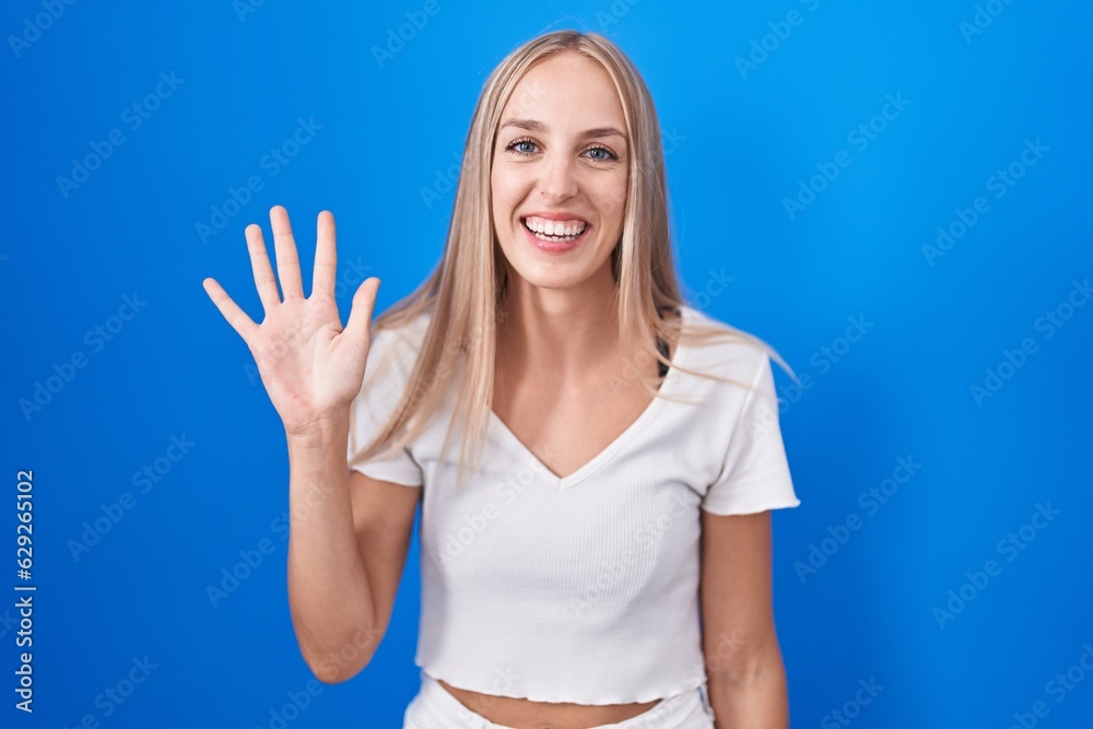 Young caucasian woman standing over blue background showing and pointing up with fingers number five while smiling confident and happy. Young caucasian woman standing over blue background showing and pointing up with fingers number five while smiling confident and happy.
