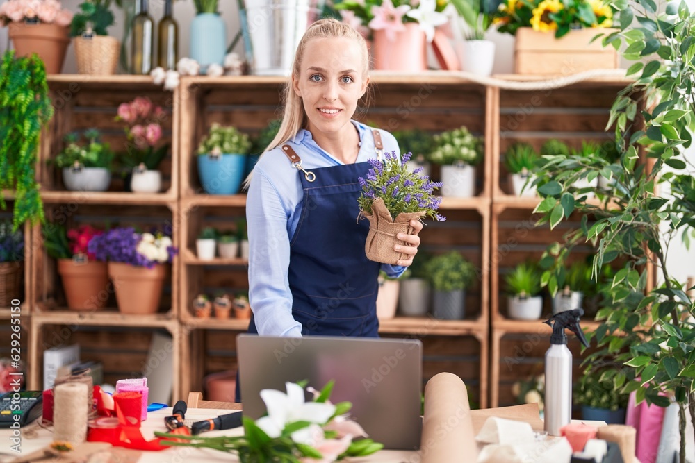 Young blonde woman florist using laptop holding lavender plant at florist