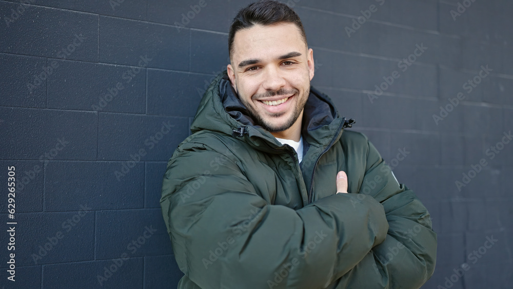 Fototapeta premium Young hispanic man smiling confident standing with arms crossed gesture over isolated black background