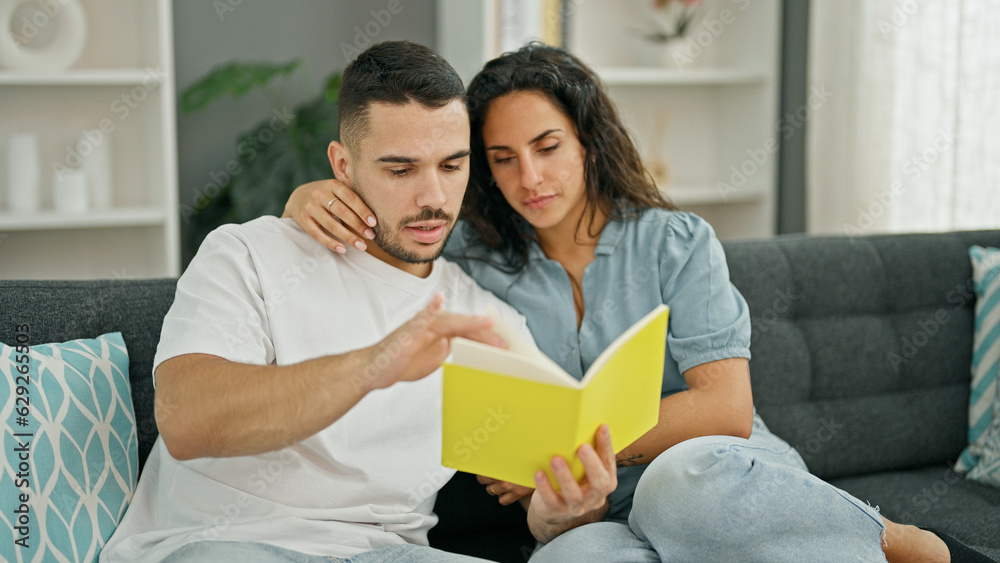 Man and woman couple reading book sitting on sofa at home Man and woman couple reading book sitting on sofa at home