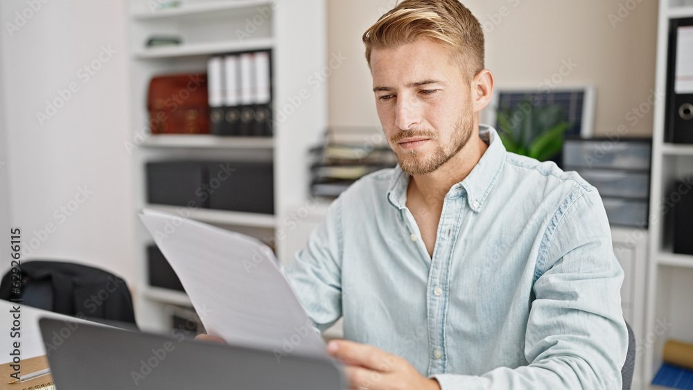 Young caucasian man business worker using laptop reading document at office Young caucasian man business worker using laptop reading document at office