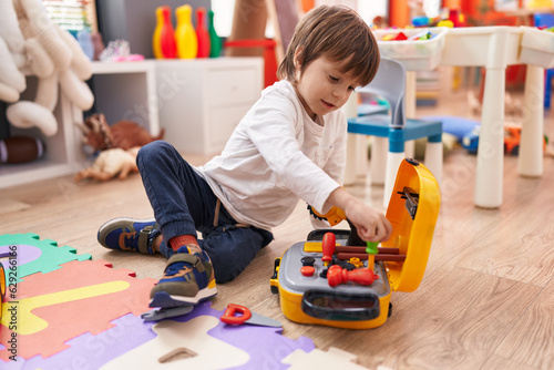 Adorable caucasian boy playing with tools toy sitting on floor at kindergarten