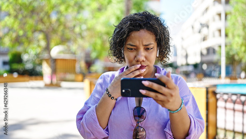 Young beautiful latin woman watching video on smartphone looking upset at park