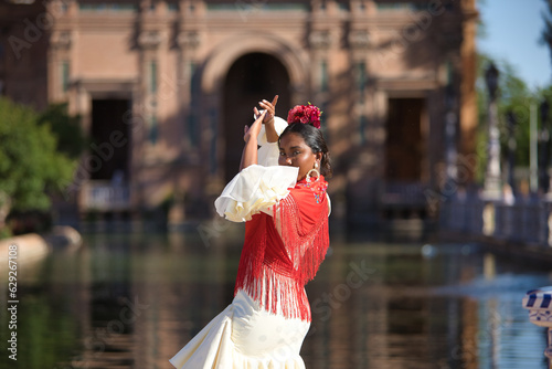 Young black and South American woman in a beige gypsy flamenco suit and red shawl, dancing in a beautiful square in the city of Seville in Spain. Concept dance, folklore, flamenco, art.