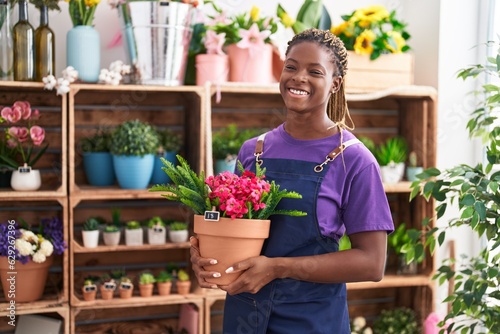 African american woman florist smiling confident holding plant at florist