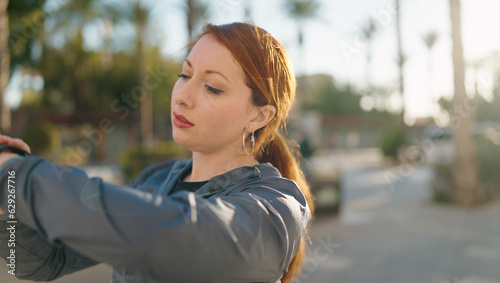 Young redhead woman wearing sportswear looking stopwatch at street photo