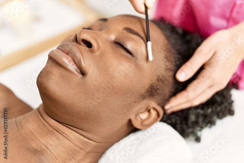 African american woman lying on massage table having eyebrows treatment at beauty salon