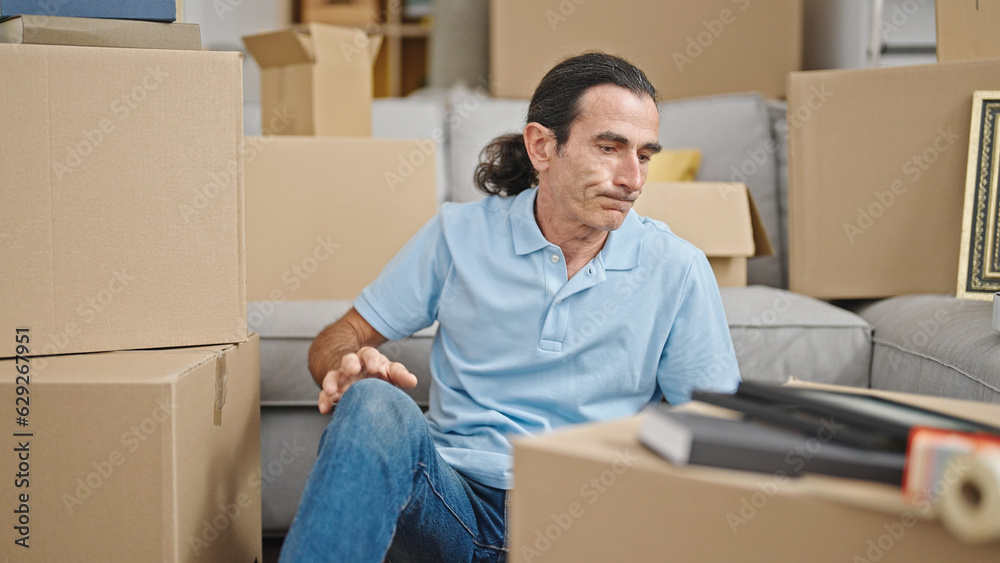 Middle age man sitting on floor looking around at new home Middle age man sitting on floor looking around at new home