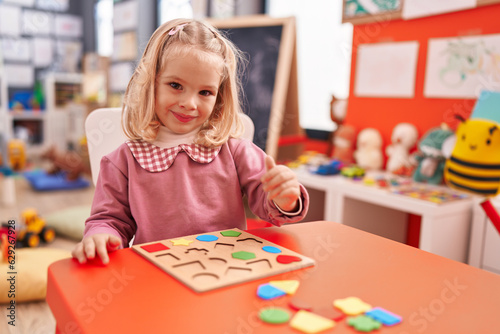 Adorable blonde girl playing with maths puzzle game at kindergarten