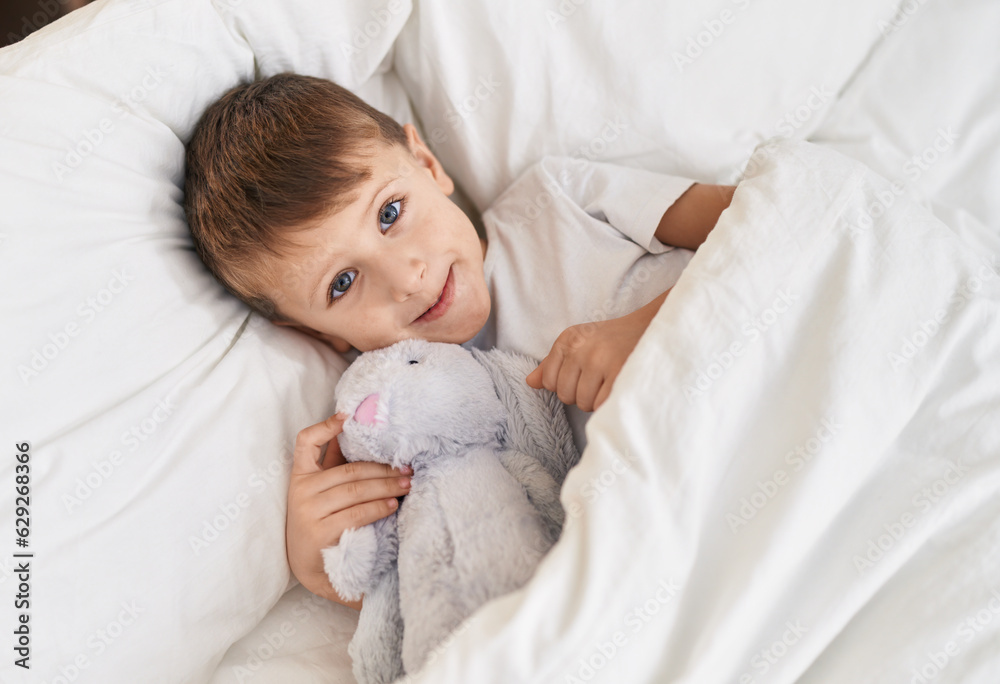 Adorable caucasian boy lying on bed with doll at bedroom Adorable caucasian boy lying on bed with doll at bedroom