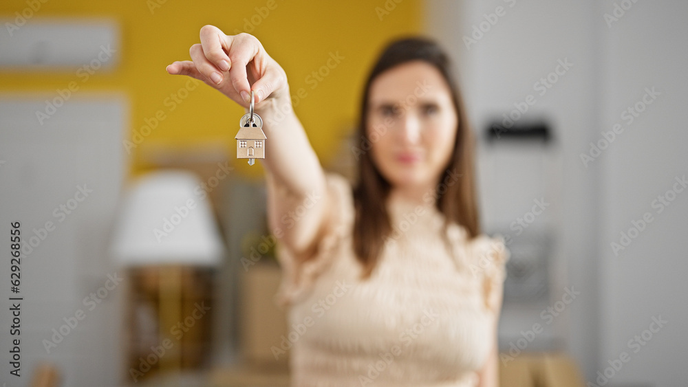 Young beautiful hispanic woman holding new house keys at new home