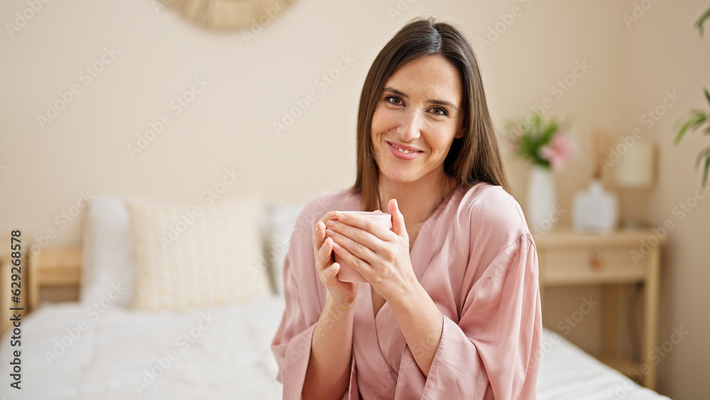 Young beautiful hispanic woman drinking cup of coffee sitting on bed at bedroom Young beautiful hispanic woman drinking cup of coffee sitting on bed at bedroom