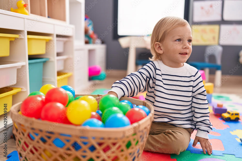 Obraz premium Adorable caucasian boy playing with balls sitting on floor at kindergarten