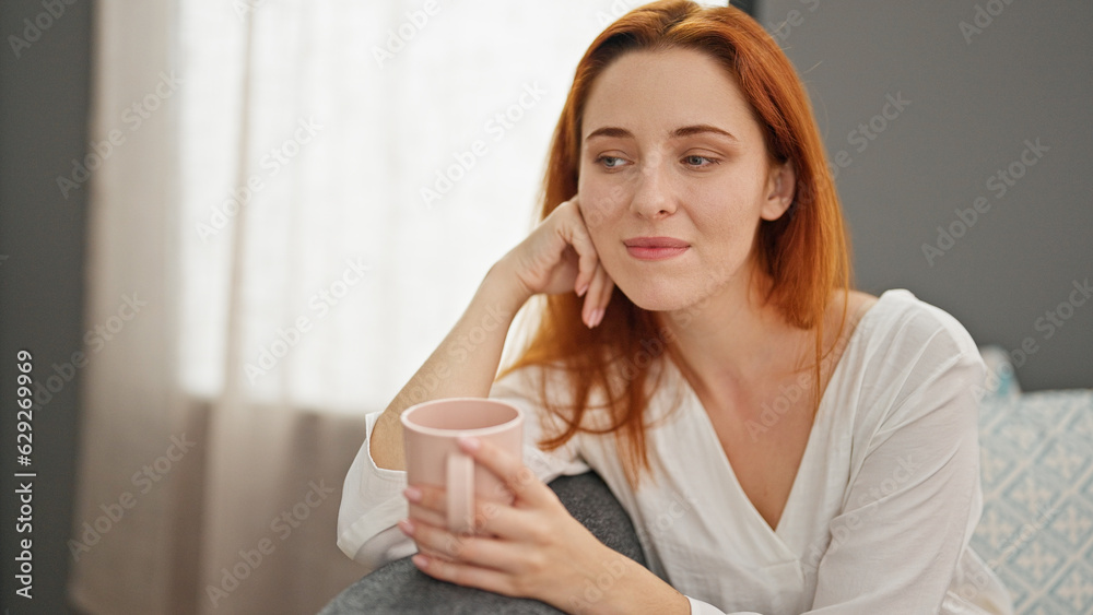 Young redhead woman drinking coffee sitting on sofa at home Young redhead woman drinking coffee sitting on sofa at home