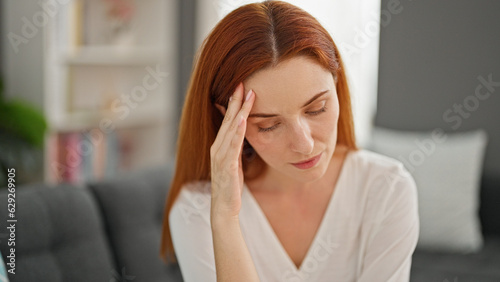 Young redhead woman stressed sitting on sofa at home